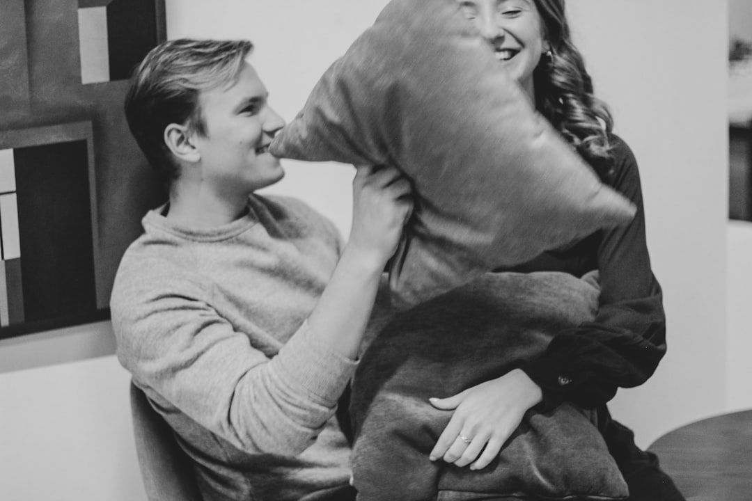 grayscale photography of man and woman pillow fighting