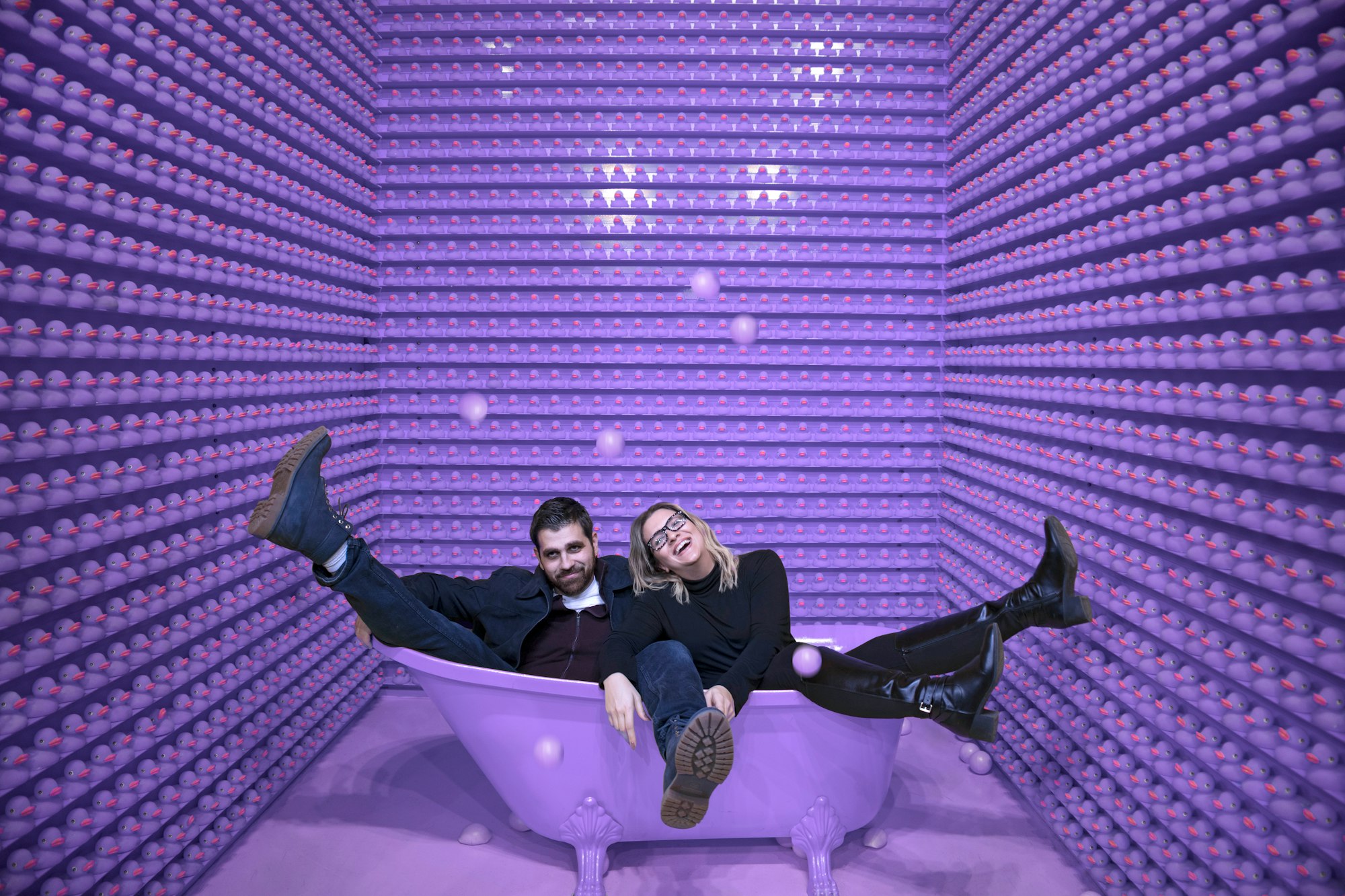 man and woman sitting in a purple bathtub