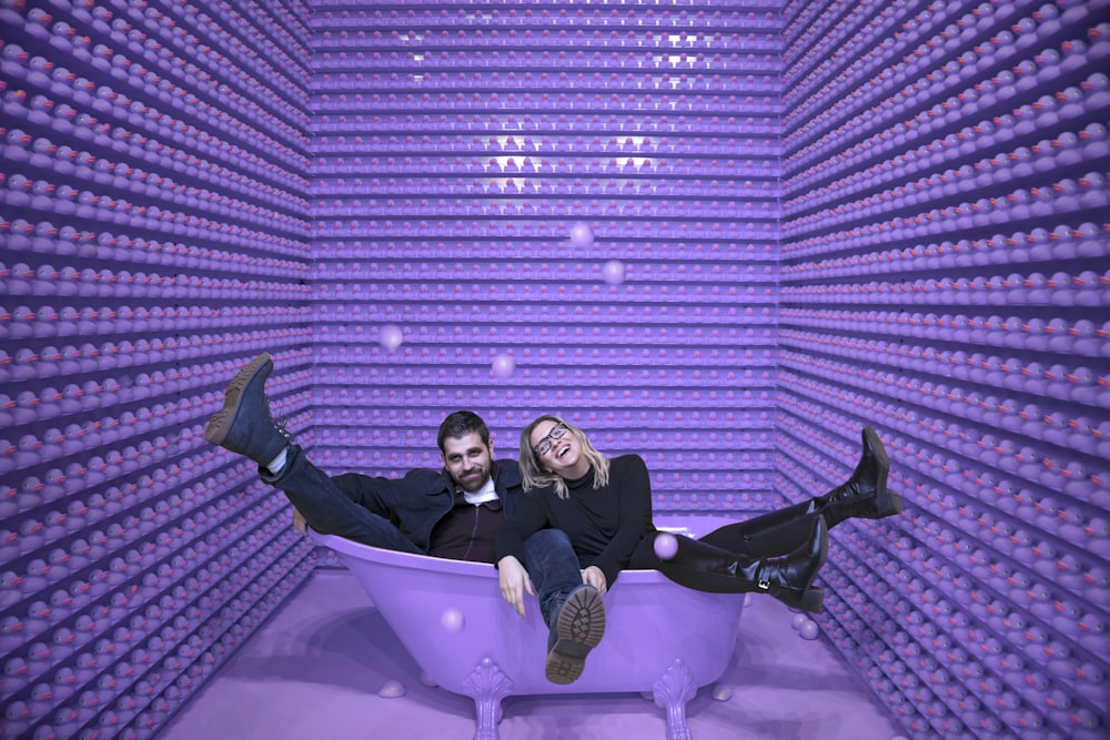 man and woman sitting in a purple bathtub