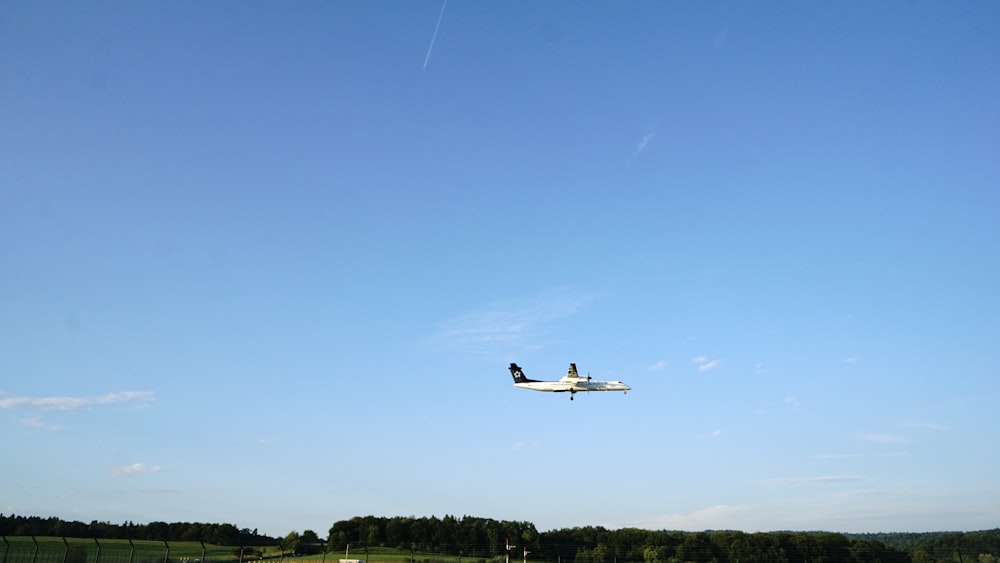 white commercial plane flying over trees during daytime