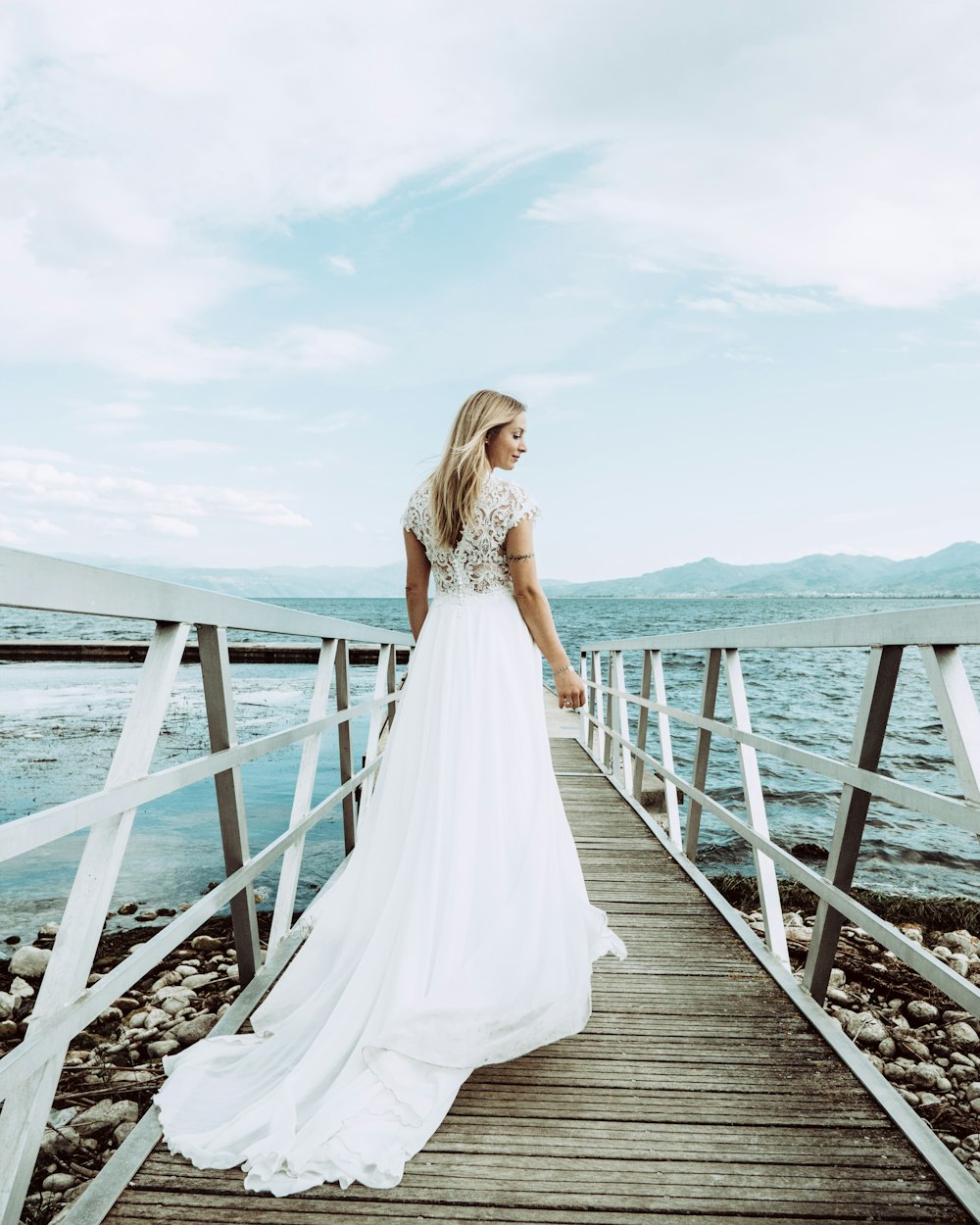 woman in white dress standing on dock bridge near seashore