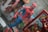 A detailed figurine of a superhero in a red and blue costume with a black spider emblem on the chest. The figure stands in a dynamic pose with one arm slightly forward. Surrounding it are various comic-themed items, including a book with vibrant illustrations.