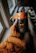 A close-up of a hand holding a bright orange ceramic mug with a cozy knitted sweater in the background.