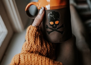 person holding orange and gray skull print ceramic mug
