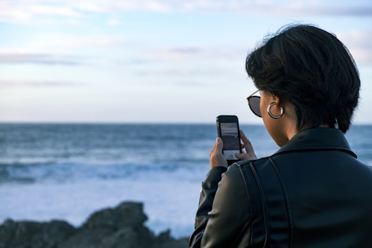 woman standing while using phone during daytime in Praia do Guincho Portugal