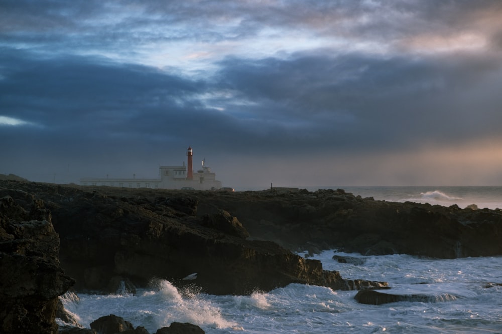 Rot-weißer Leuchtturm auf Klippen mit Blick auf das Meer unter blauem und weißem Himmel während des Tages