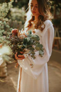 Bride holding a lush bouquet of hollyhocks and mixed flowers in soft sunlight
