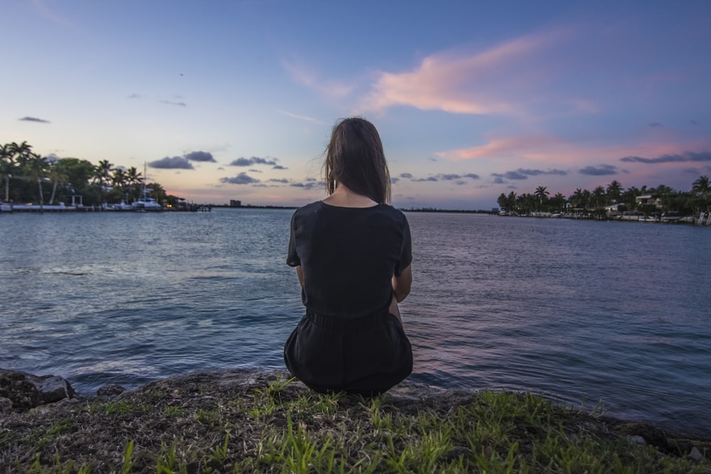 woman sitting on grass overlooking body of water