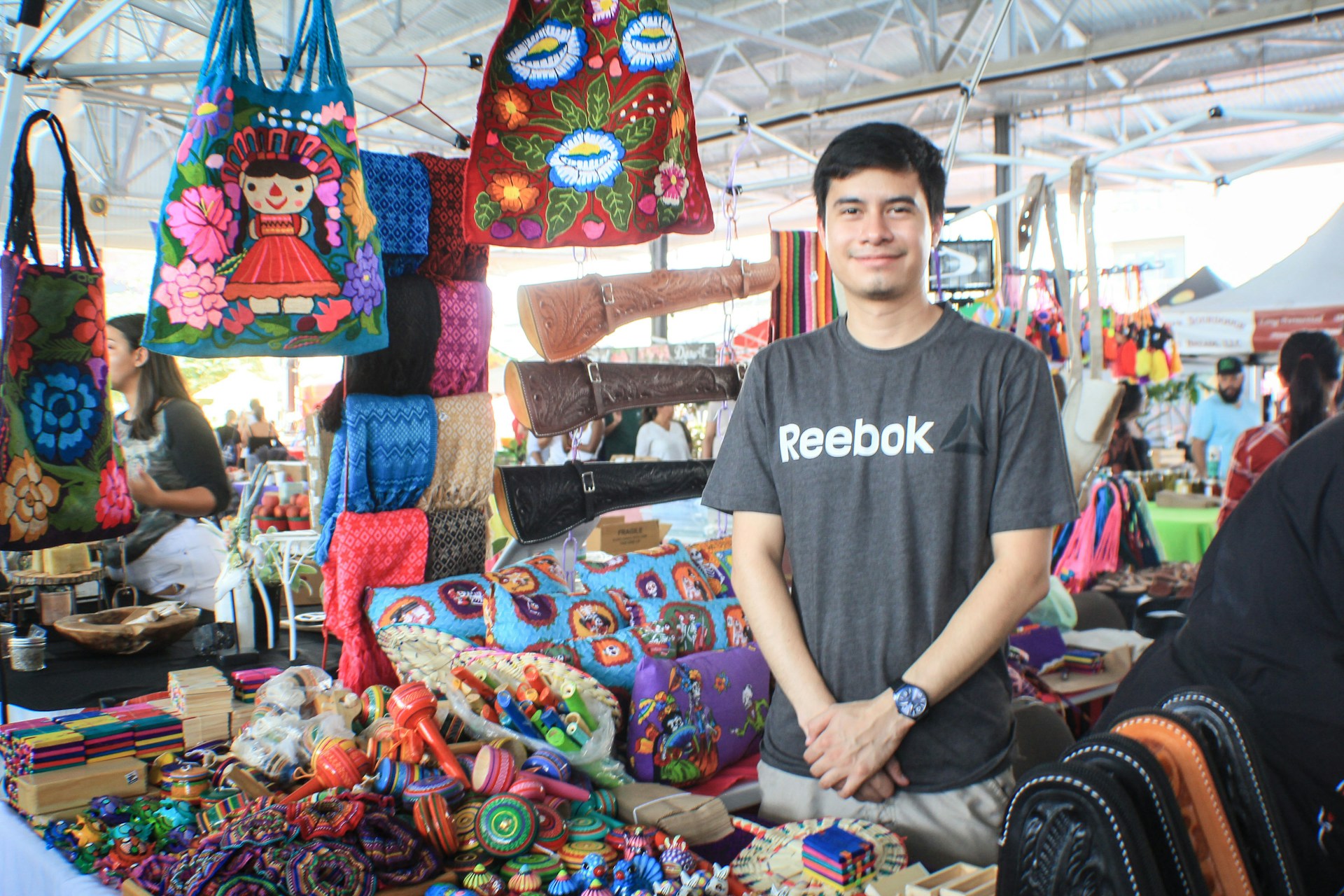 An artisan demonstrating local crafts with colorful handmade goods displayed at a bustling festival market stall.