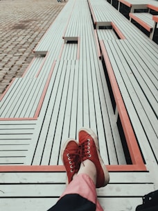 Bright red rubber slip-on shoes resting on a sunny park bench.