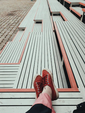 Pair of vibrant red and white casual sneakers resting on a wooden bench in a park.