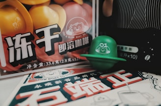A variety of colorful pods are displayed, featuring bright yellows, oranges, and greens. The pods are part of a promotional setup with Chinese characters and playful graphics on the packaging. The composition includes a green pod prominently placed in the foreground, branded with a smiling character design.