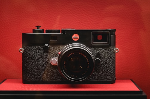 Close-up of a retro camera with bold red and black coloring against a simple backdrop.