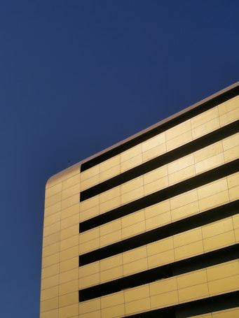 A modern building with a facade featuring horizontal black slats set against a golden-yellow wall, captured under a clear blue sky.
