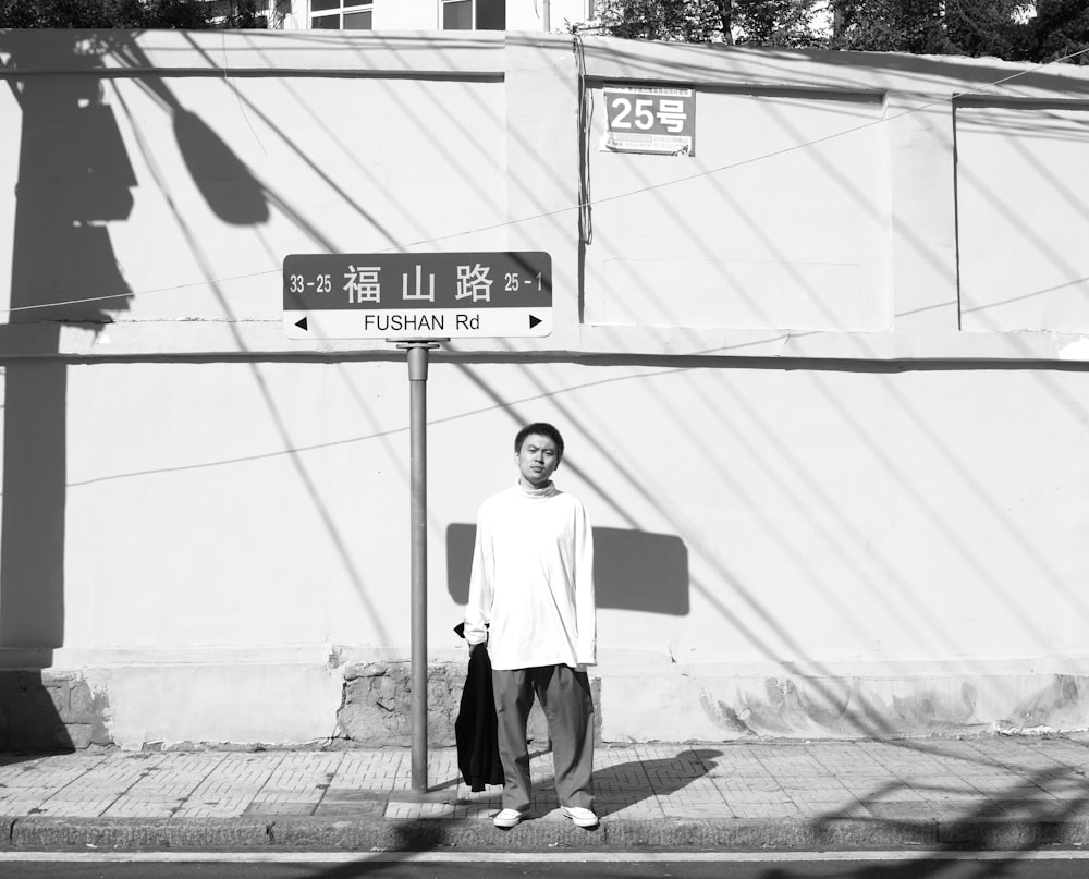 man standing near street post grayscale photo