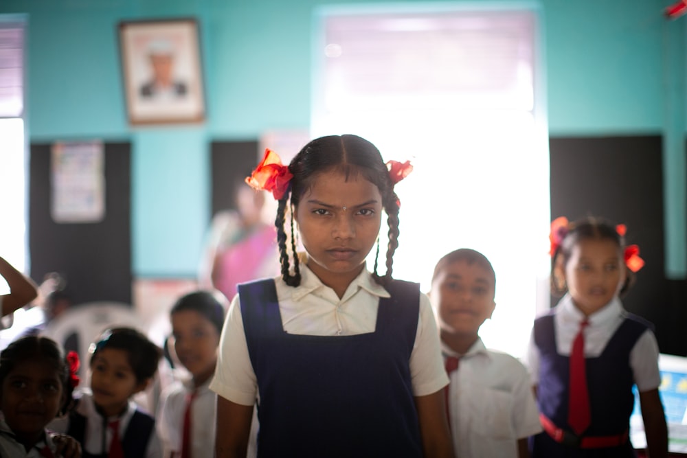 Selektive Fokusfotografie eines stehenden Mädchens in Uniform in einem blau gestrichenen Raum mit Klassenkameraden