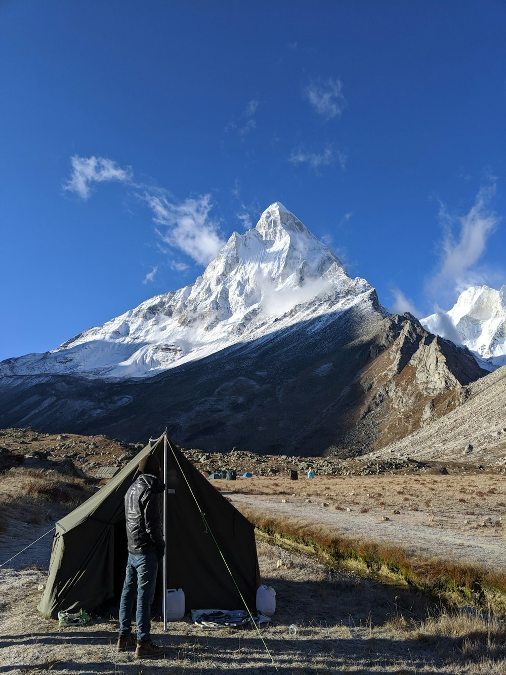 man standing beside tent under blue sky