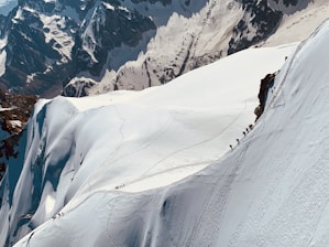 Climbers ascending a snowy Himalayan peak under a clear blue sky.