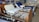 A room containing several hospital beds, some with attached bedside tables. The beds are equipped with adjustable rails and various types of mattresses. The room has posters and shelves lining the walls, filled with various medical and bedding supplies.