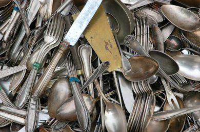 A collection of mixed metal cutlery including silver and stainless steel pieces.