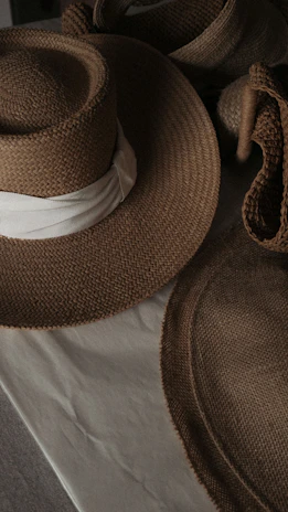 Softly lit close-up of satin bonnets and delicate hats arranged on a beige fabric.