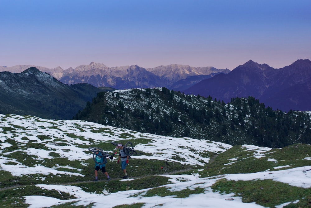 two men carrying bicycle walking on mountain