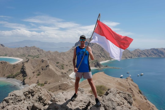 man with flag standing on hill during daytime in Komodo National Park Indonesia