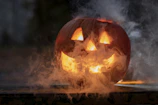 A glowing jack-o'-lantern surrounded by flickering candles on a foggy night.
