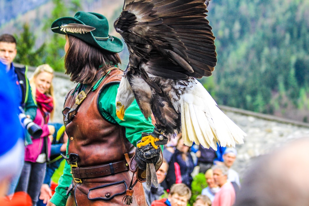 woman wearing brown leather vest and green with eagle pearched on her hand