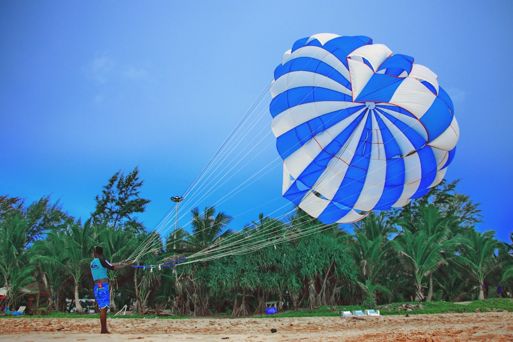 man standing while holding blue and white parachute under blue and white sky during daytime