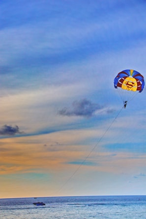 A parasailer soaring high above the ocean, with the shoreline and boats visible far below.