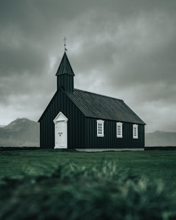 white and black wooden church on green field viewing mountain during daytime