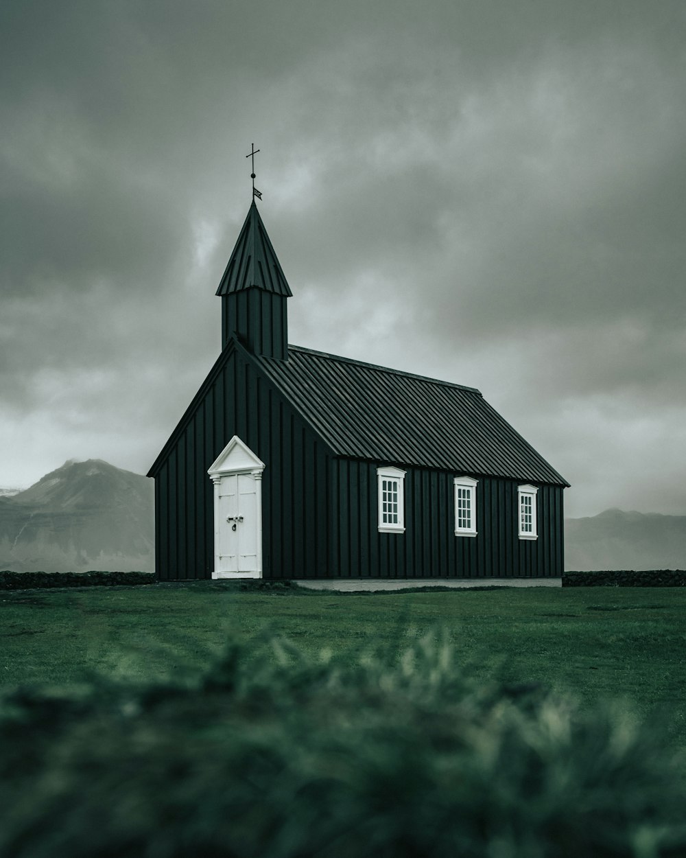 white and black wooden church on green field viewing mountain during daytime