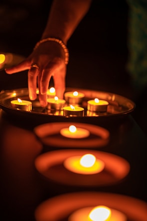 A close-up of hands performing a traditional astrology ritual with candles and sacred items glowing in gold hues.
