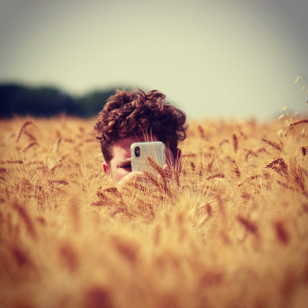 man holding silver iPhone X surrounded by grass