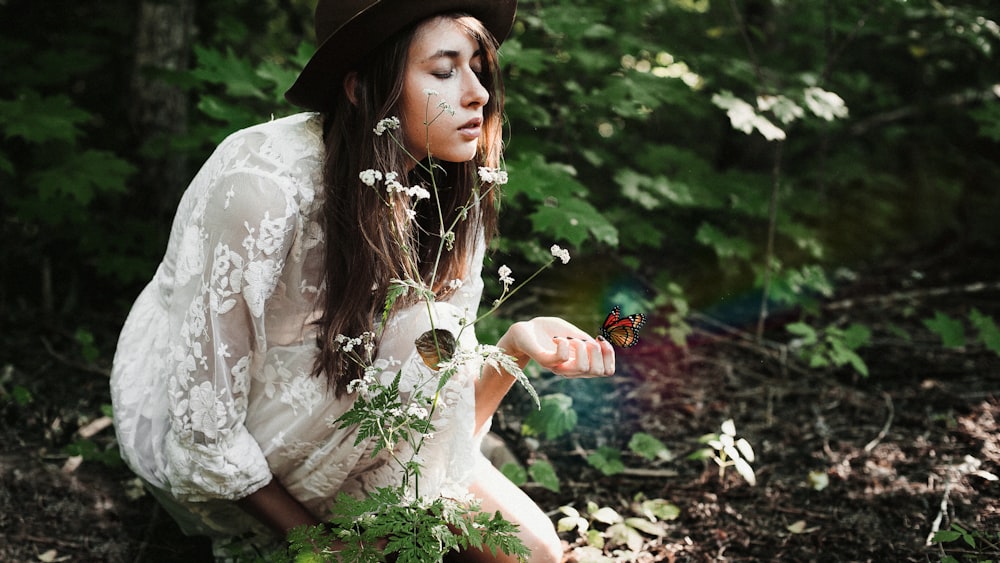 woman wearing white lace long-sleeved dress sniffing petaled flower