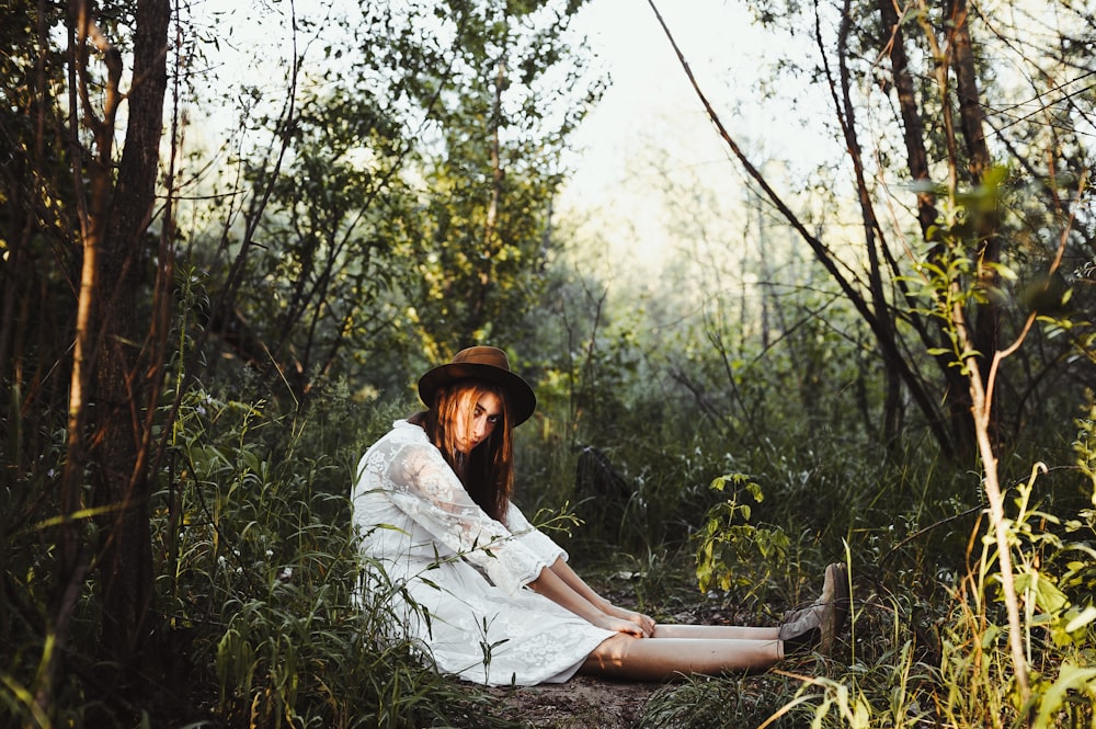 woman in white dress sitting surrounded by trees and grass during daytime