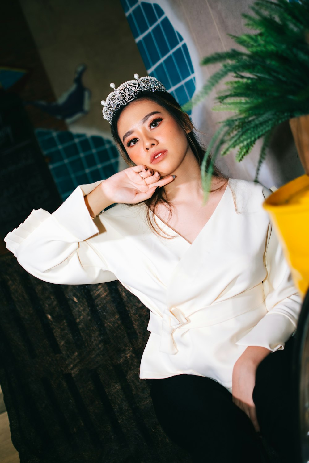 woman wearing white V-neck long-sleeved blouse and silver crown sitting while touching her face