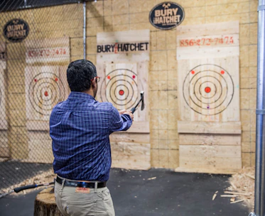 A group of friends enthusiastically throwing axes in a dimly lit, modern indoor axe-throwing venue.