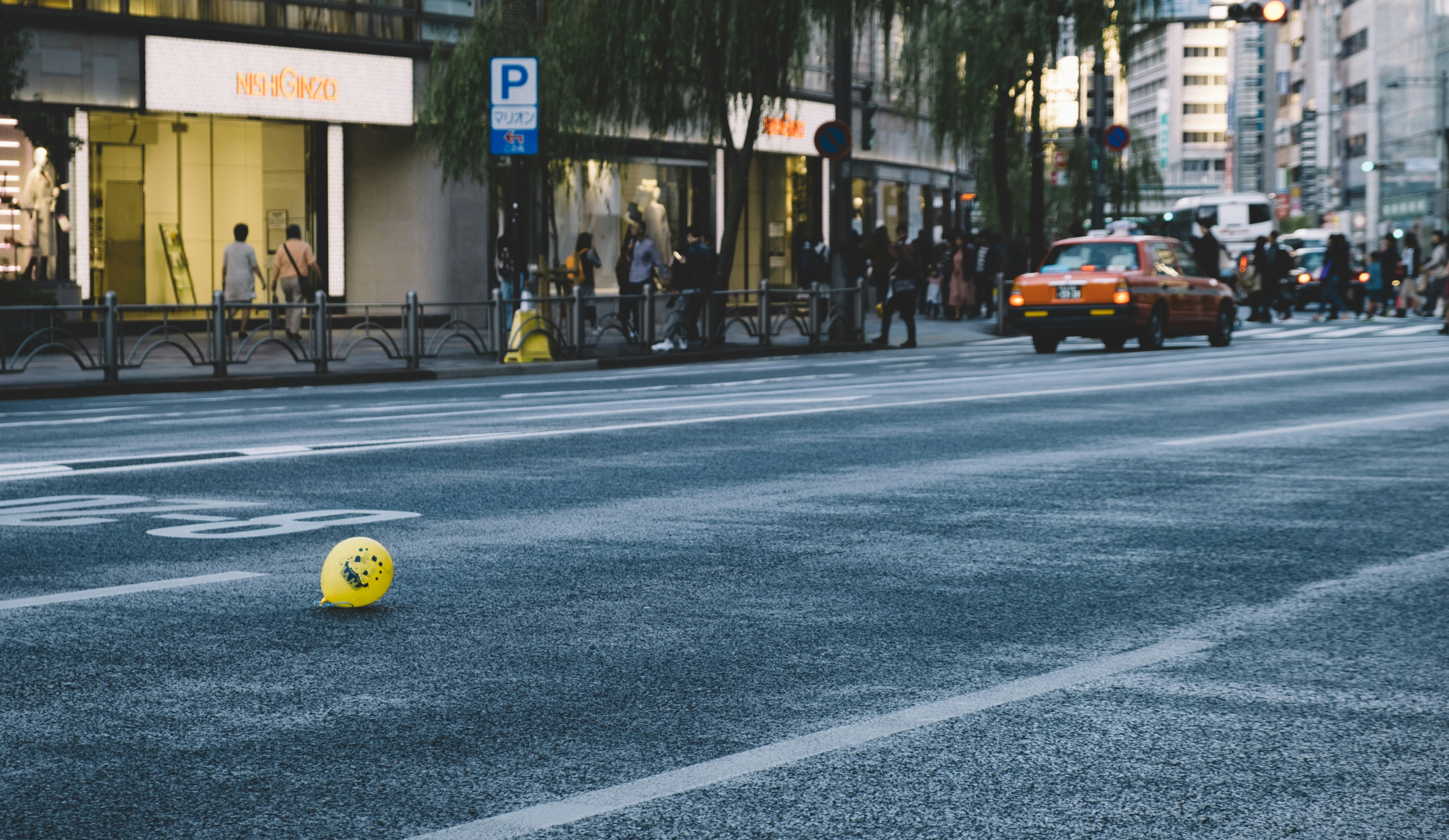 people walking on pathway near buildings and few vehicles on road during daytime