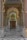 A person is sweeping the floor in a beautifully decorated corridor with intricate designs and vibrant colors. The corridor is detailed with floral and geometric patterns, and there is an ornate door at the end, surrounded by traditional Indian architecture elements.