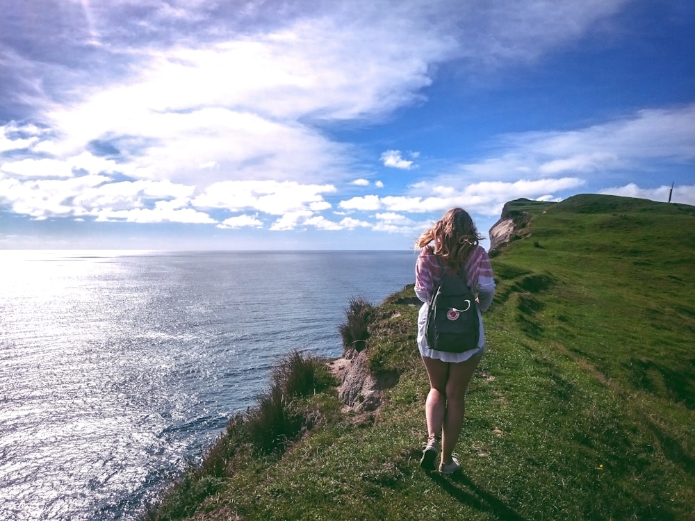 woman standing on cliff near body of water during daytime