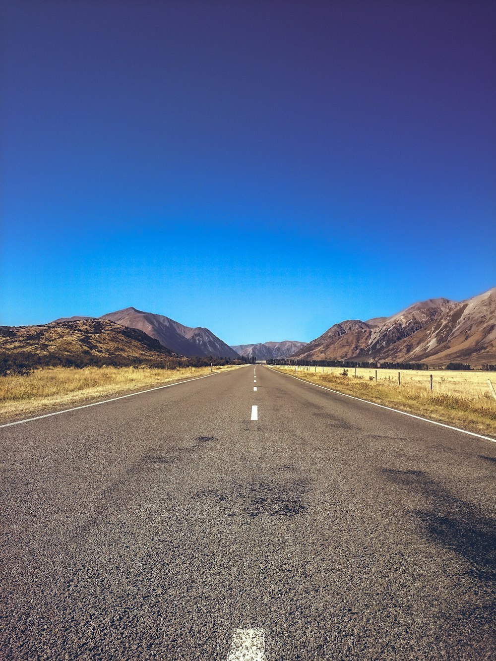 empty road between plain field under blue sky