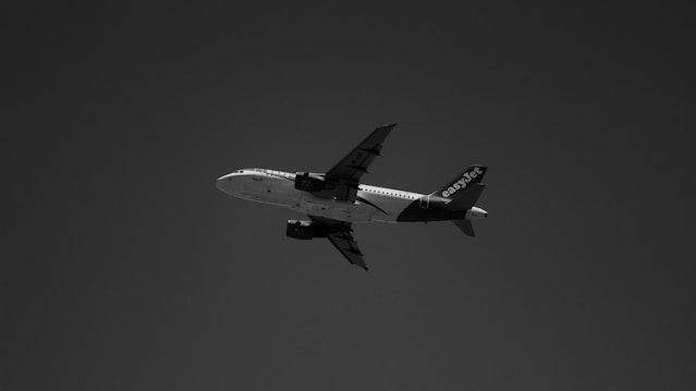 A black and white photograph of an airplane flying against a dark sky. The aircraft is seen from a low angle with the wings and tail visible. The word 'easyJet' is prominently displayed on the tail.