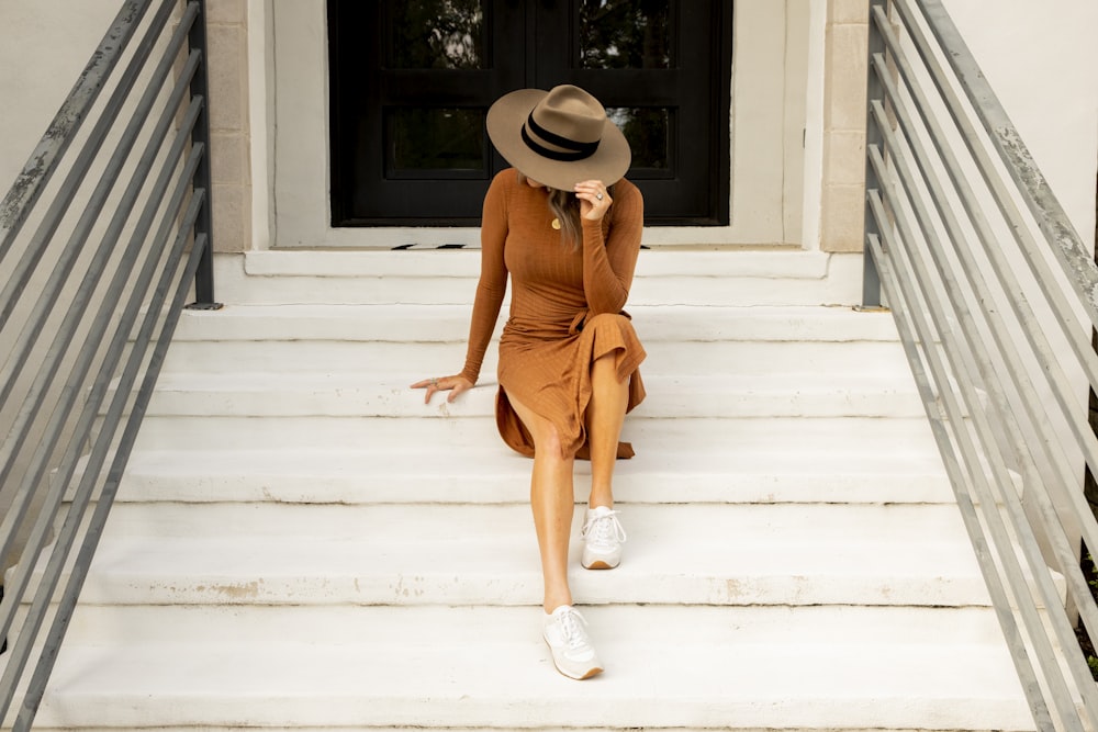 woman in brown dress wearing sun hat while sitting on stare during daytime