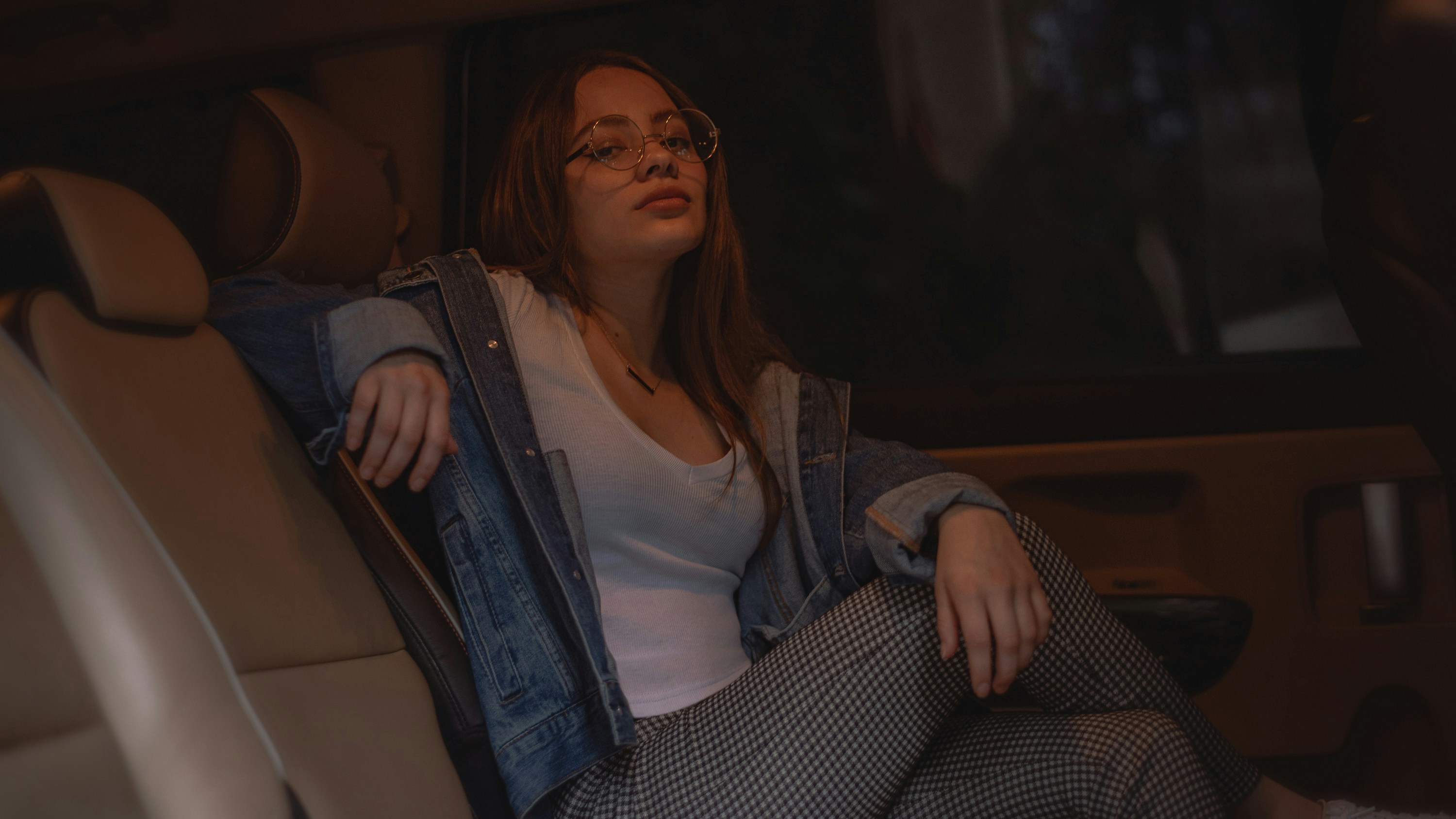 Frau in weißem Oberteil, blauer Jeansjacke und grauer Hose sitzt im Fahrzeug