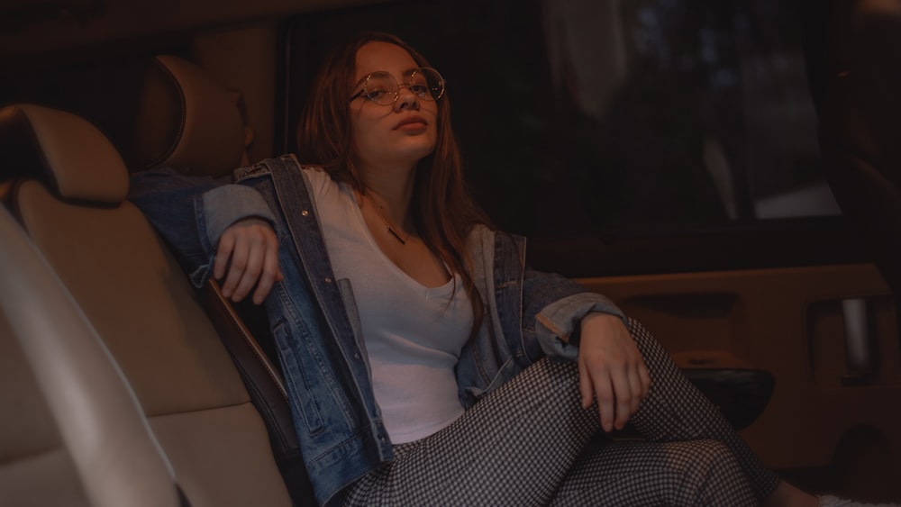 woman in white top, blue denim jacket, and gray pants sitting inside vehicle