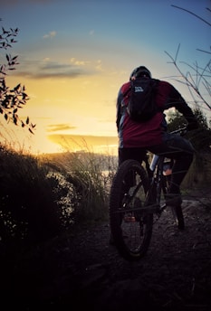 Happy cyclist riding a boosted bike on a scenic trail with a sunset backdrop.