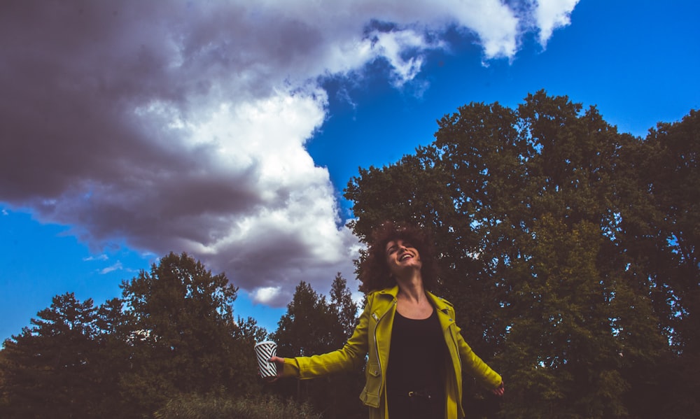 smiling woman wearing green jacket beside trees