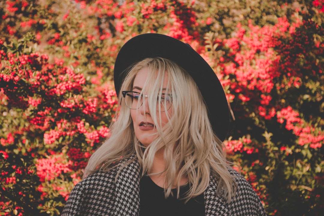 woman with hat standing near red petaled flowers during daytime